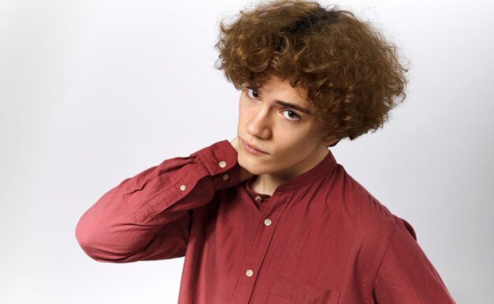 Men’s hairstyle featuring voluminous natural curls on top with a clean drop fade curving behind the ears.