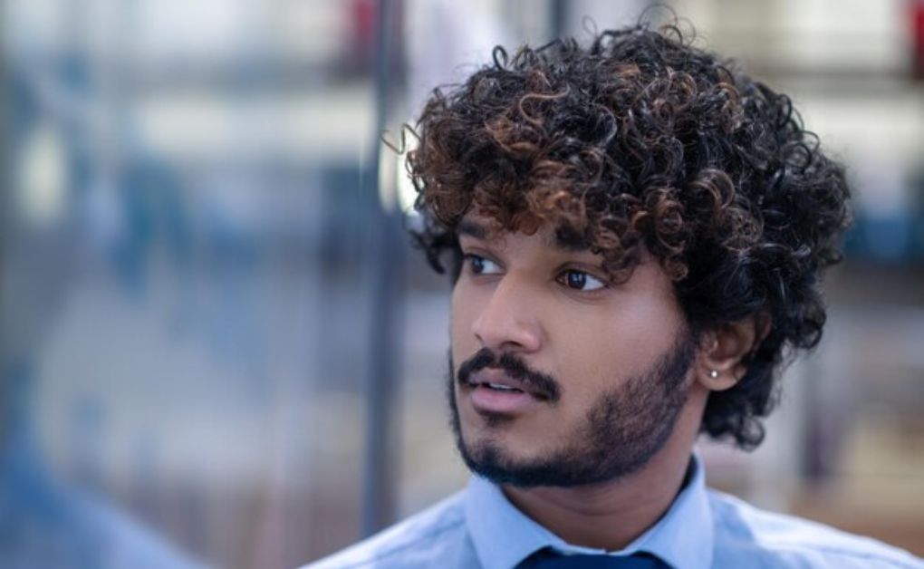 Men’s short natural curls styled with a clean low taper fade around the sideburns and neckline.